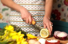 en person som skär upp en citron och har en arbetsbänk fylld med grönsaker och blommor